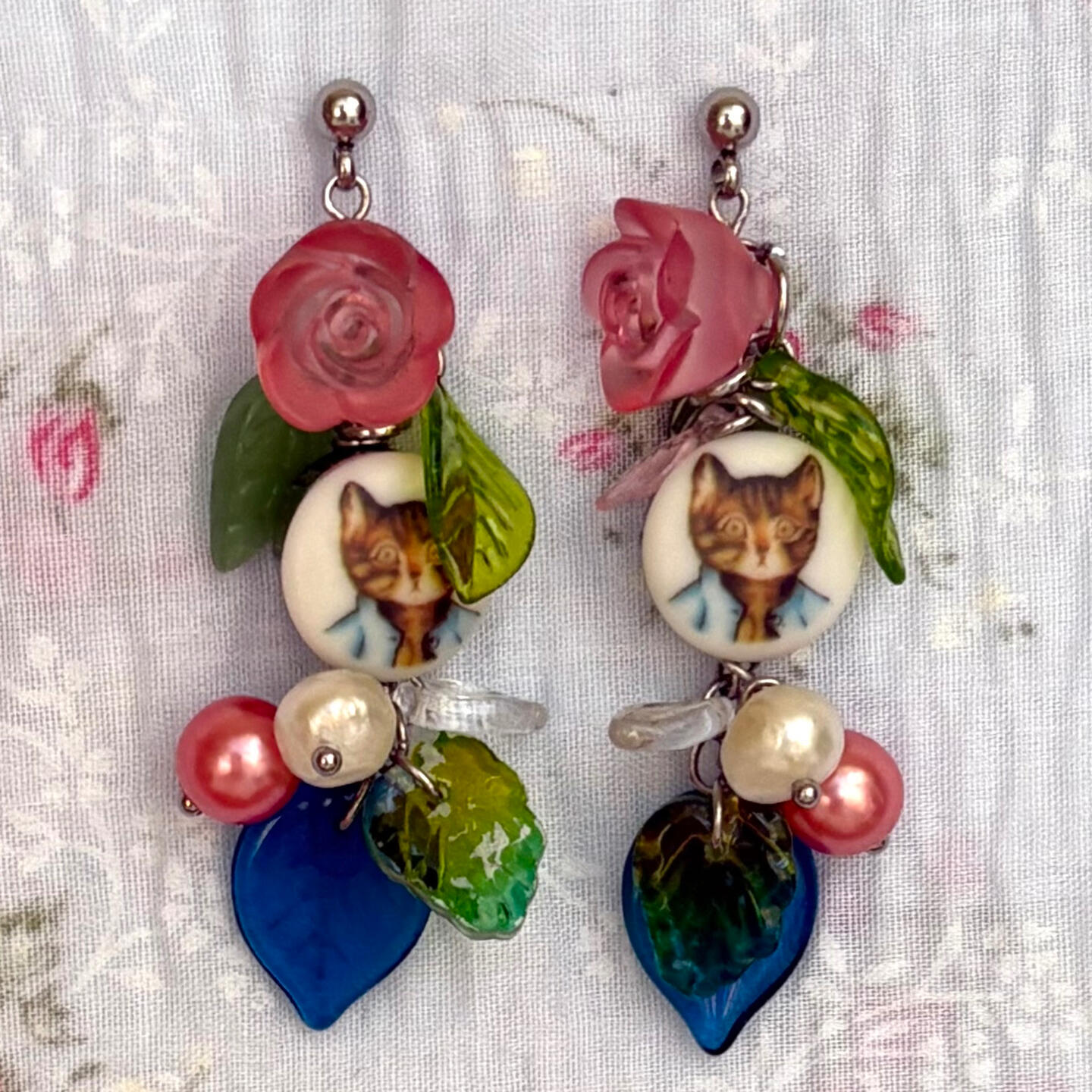 trot home, just in time for supper. this earring pair pays homage to a well loved illustrator, a re-imagination of a world adored by many. featuring tom kitten buttons, czech glass leaves, acrylic roses, freshwater pearls, and stainless steel hardware.